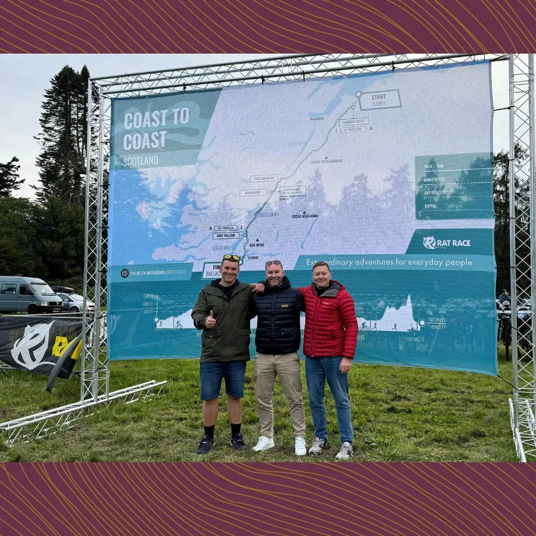 Three men posing in front of Coast to Coast Scotland event map at Rat Race outdoor adventure.
