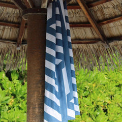 Blue and white striped beach towel hanging on tiki hut by tropical greenery