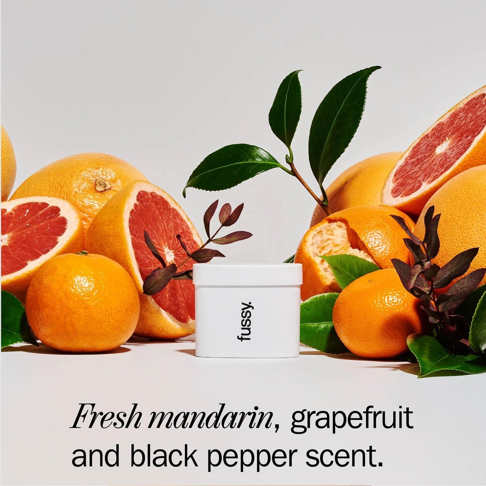 Fussy deodorant with fresh mandarins, grapefruits, and green leaves in a bright setting