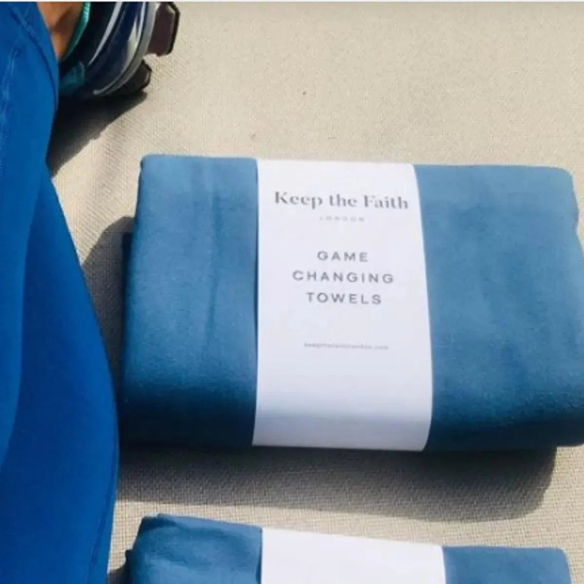 Folded blue Keep the Faith game changing towels on beige fabric, sports shoe visible