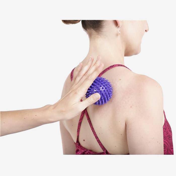 Hand using purple spiky massage ball on woman's upper back for muscle relief