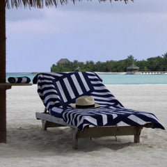 Navy and white geometric beach towel on lounge chair by ocean with hat, tropical setting