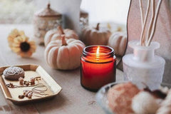 Autumn decor with white pumpkins, jewelry tray, and a lit candle on wooden table