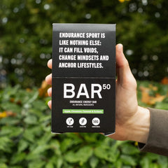 Hand holding BAR50 endurance energy bar box with vegan, gluten free, apple cinnamon flavors