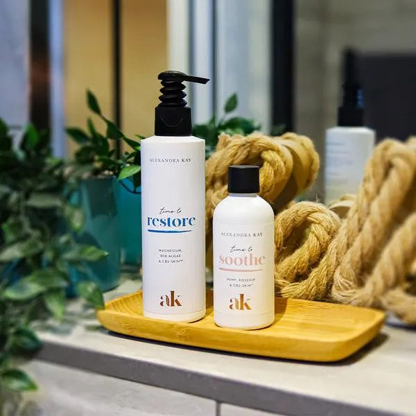 Alexandra Kay magnesium lotion bottles on a wooden tray with rope and plants by a mirror