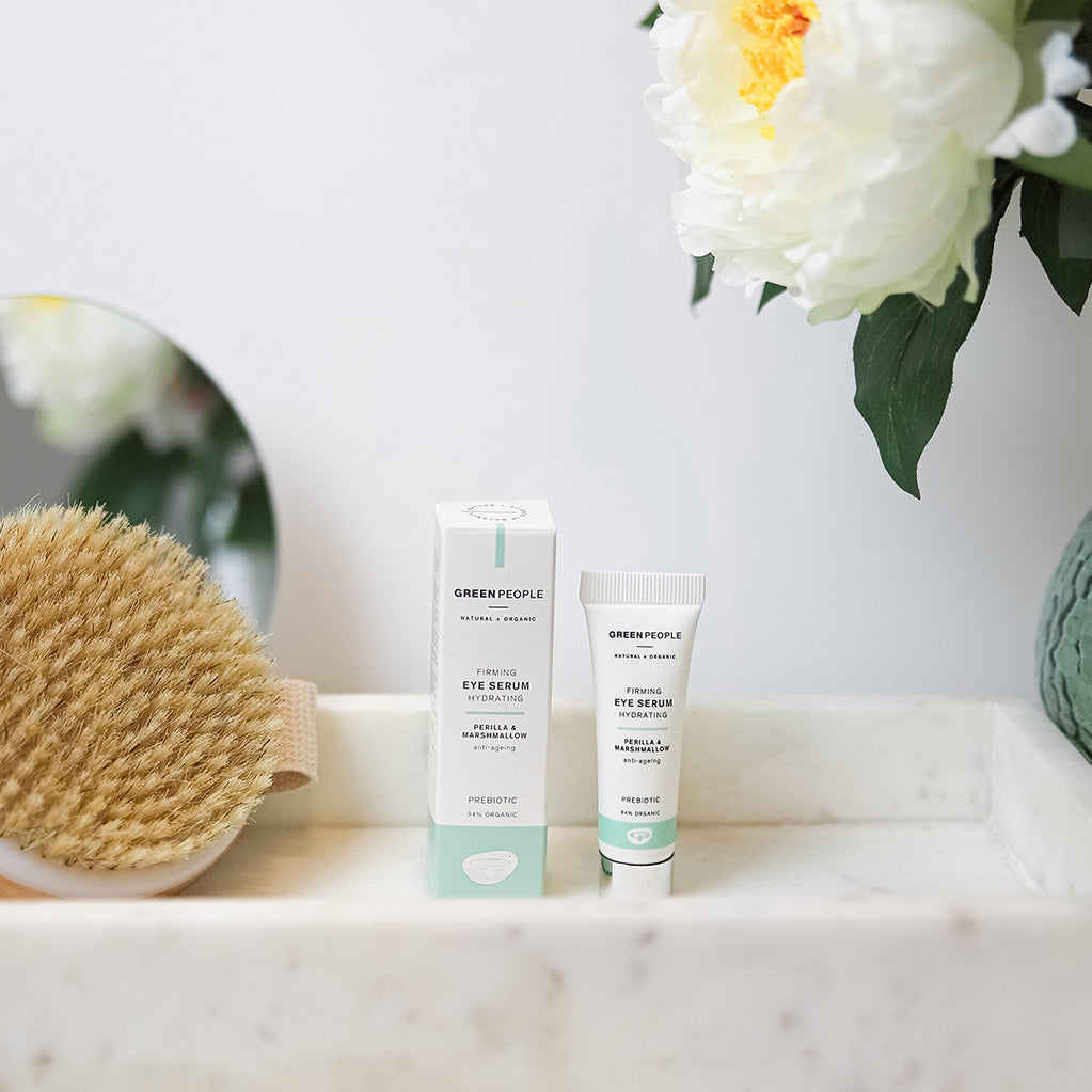 Green People Firming Eye Serum and box on marble tray with body brush and white peony flower