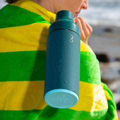 Forest green reusable water bottle on yellow and green towel at the beach