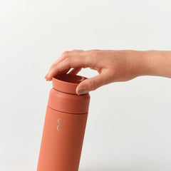 Hand opening Sahara Red Brew 350ml reusable coffee cup against white background