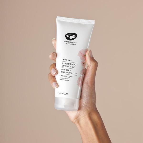 Hand holding Green People Moisturising Shower Gel tube, neroli and marshmallow, on beige background