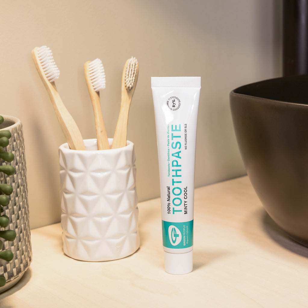 Natural toothpaste tube and bamboo toothbrushes in a ceramic holder on bathroom counter