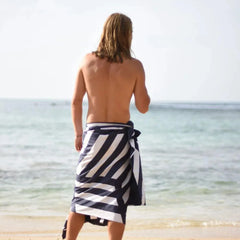 Man on beach with navy and white striped towel sarong facing the ocean