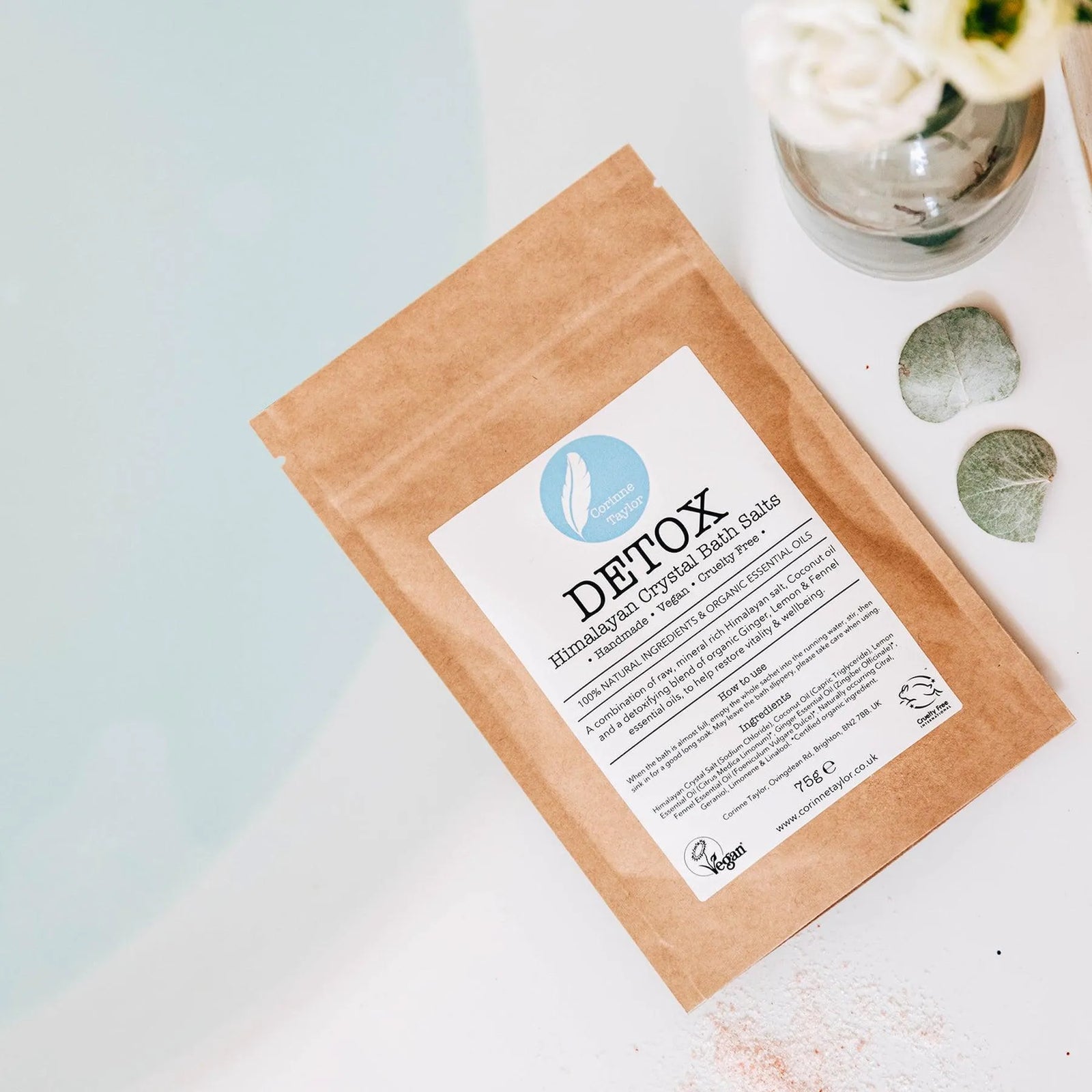 Detox Himalayan crystal bath salts pouch by a bathtub with flowers and eucalyptus leaves