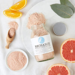 Recharge Himalayan bath salts jar with pink crystals, orange slices, grapefruit, and eucalyptus leaves