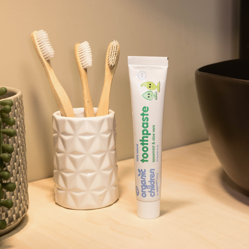 Organic children’s spearmint aloe vera toothpaste and bamboo toothbrushes on bathroom counter