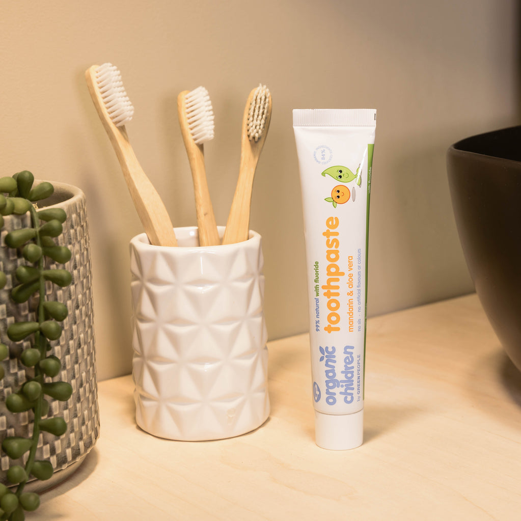 Organic children's toothpaste tube with bamboo toothbrushes in a ceramic holder on bathroom counter