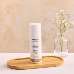 Green People scent-free facial SPF15 sun cream bottle on wood tray with vase of white flowers