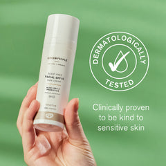 Hand holding Green People scent-free facial SPF15 sun cream bottle, dermatologically tested badge on green background