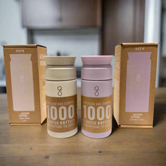 Ocean Bottle reusable water flasks in sandstone and lavender haze with packaging on wood table