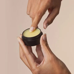 Hand applying balm from small black jar, skincare product on neutral background