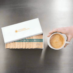 London Nootropics Mojo coffee sachets box and hand holding cup of coffee on metal table