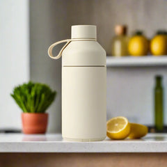 Sandstone reusable water bottle with carry loop on kitchen counter, lemon and plant nearby