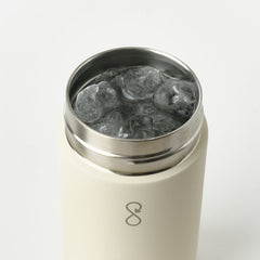 Beige insulated tumbler with stainless steel rim filled with ice, on white background