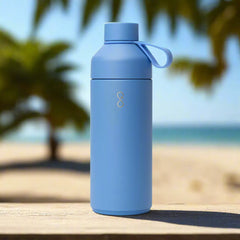 Lagoon blue water bottle on wooden table at beach with palm trees and ocean backdrop