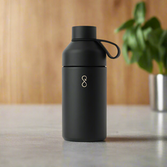 Matte black 750ml reusable water bottle with loop lid on countertop, plant blurred in background