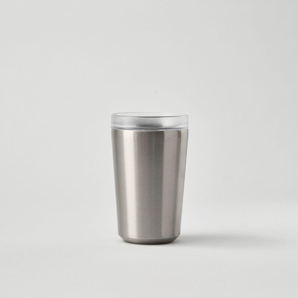 Stainless steel reusable tumbler with clear lid on plain light background