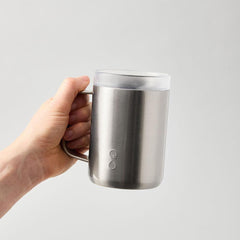 Hand holding stainless steel Ocean Bottle mug with lid on light grey background