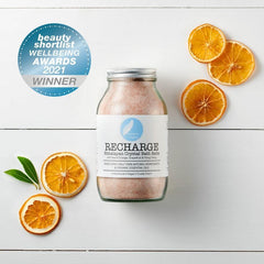 Recharge Himalayan bath salts jar with dried orange slices, award badge, white wood background