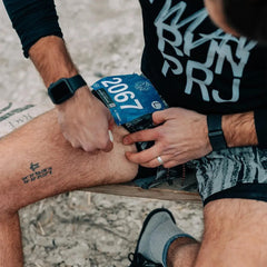 Runner applying anti-chafe stick to thigh before race, race bib 2067 visible