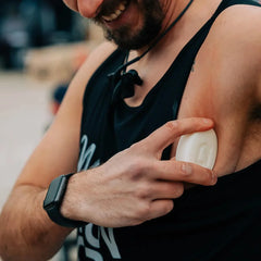 Man applying anti-chafe stick to armpit, wearing black tank top and smartwatch