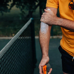 Man applying SPF 30 sun gel on arm near tennis court outdoors