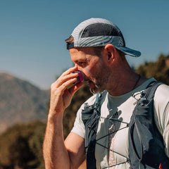 Man outdoors applying SPF 50 mineral sun stick to face, wearing cap and sport vest
