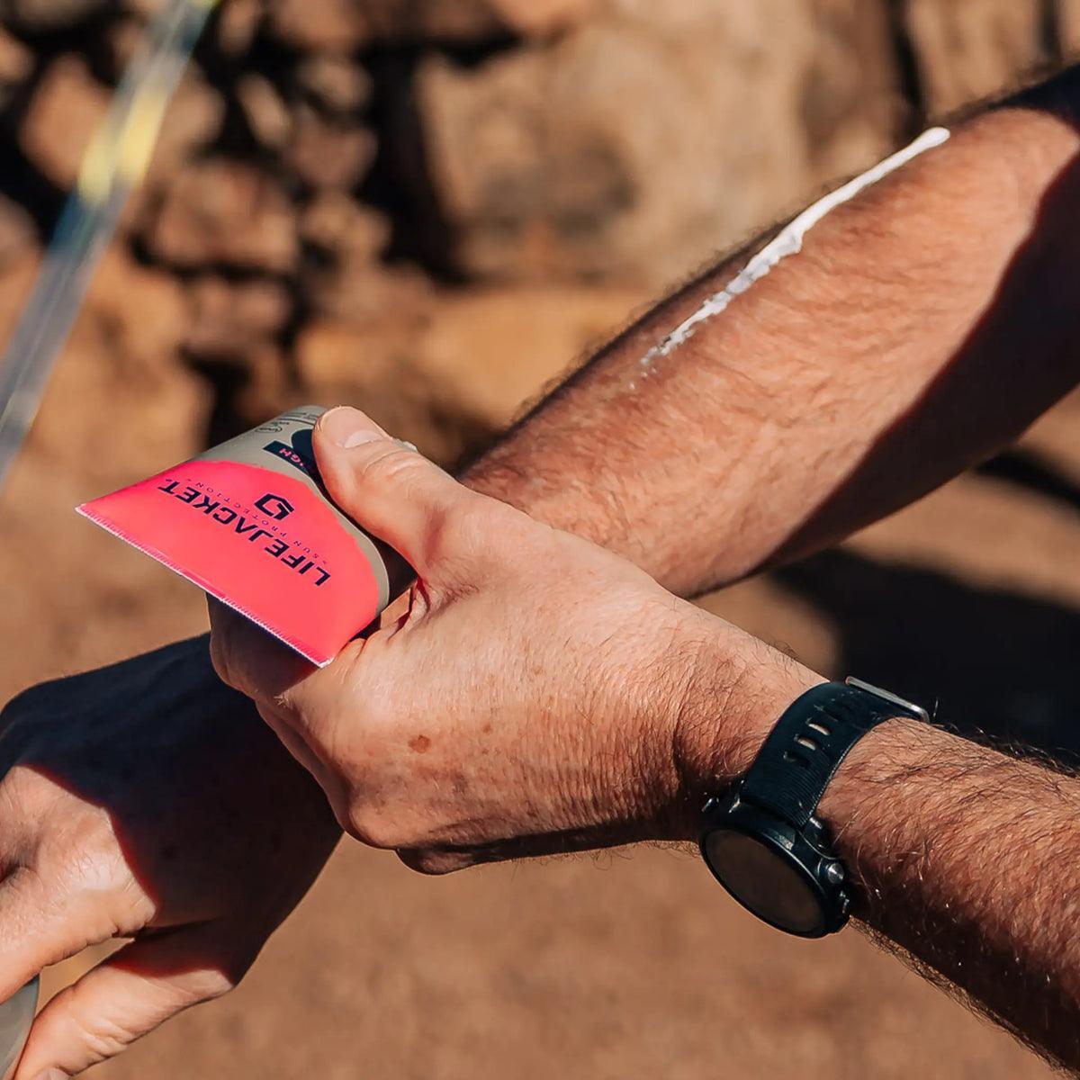 Man applying Lifekeket SPF50 Sun Gel outdoors, sunscreen on arm, rocky background
