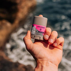 Hand holding LifeJacket Mineral Sun Stick SPF 50 by ocean on a sunny day