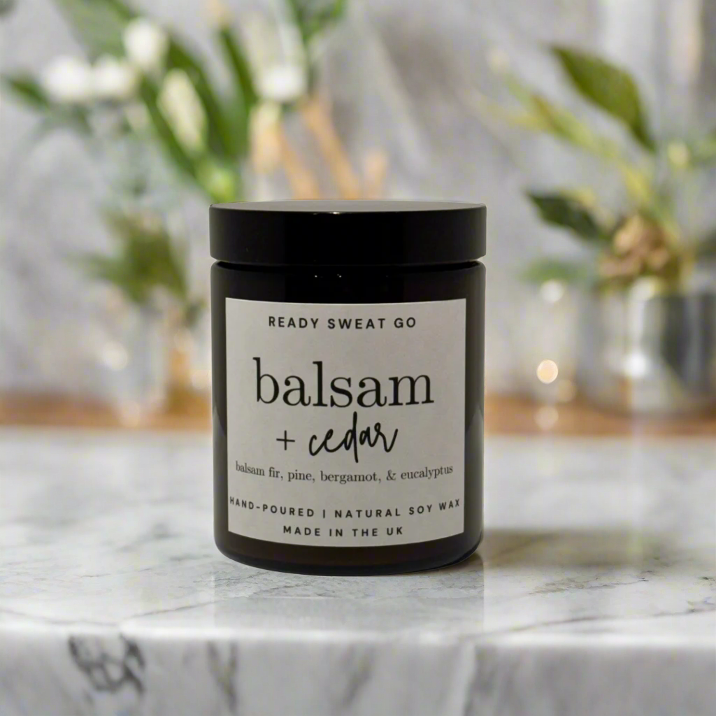 Balsam cedar natural soy wax candle in black jar on marble surface, blurred green background