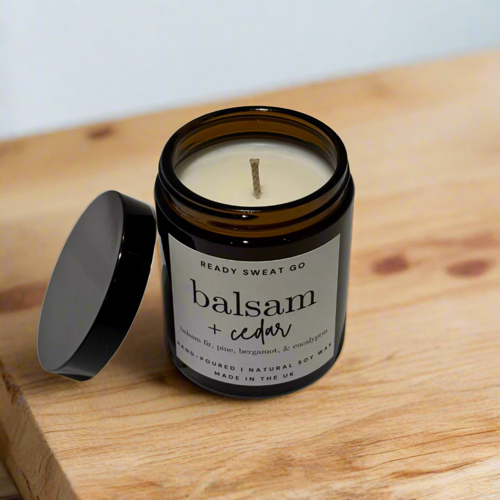 Balsam and cedar soy candle in amber jar with lid, on wooden surface