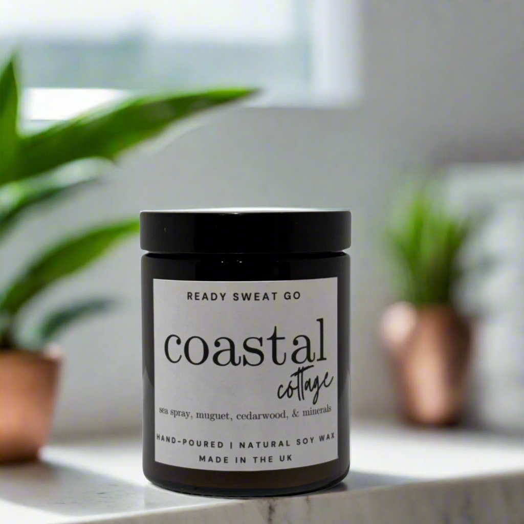 Coastal Cottage soy wax candle in black jar on marble surface with plants in background