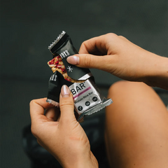 Person opening a raspberry protein rice bar in sporty setting.