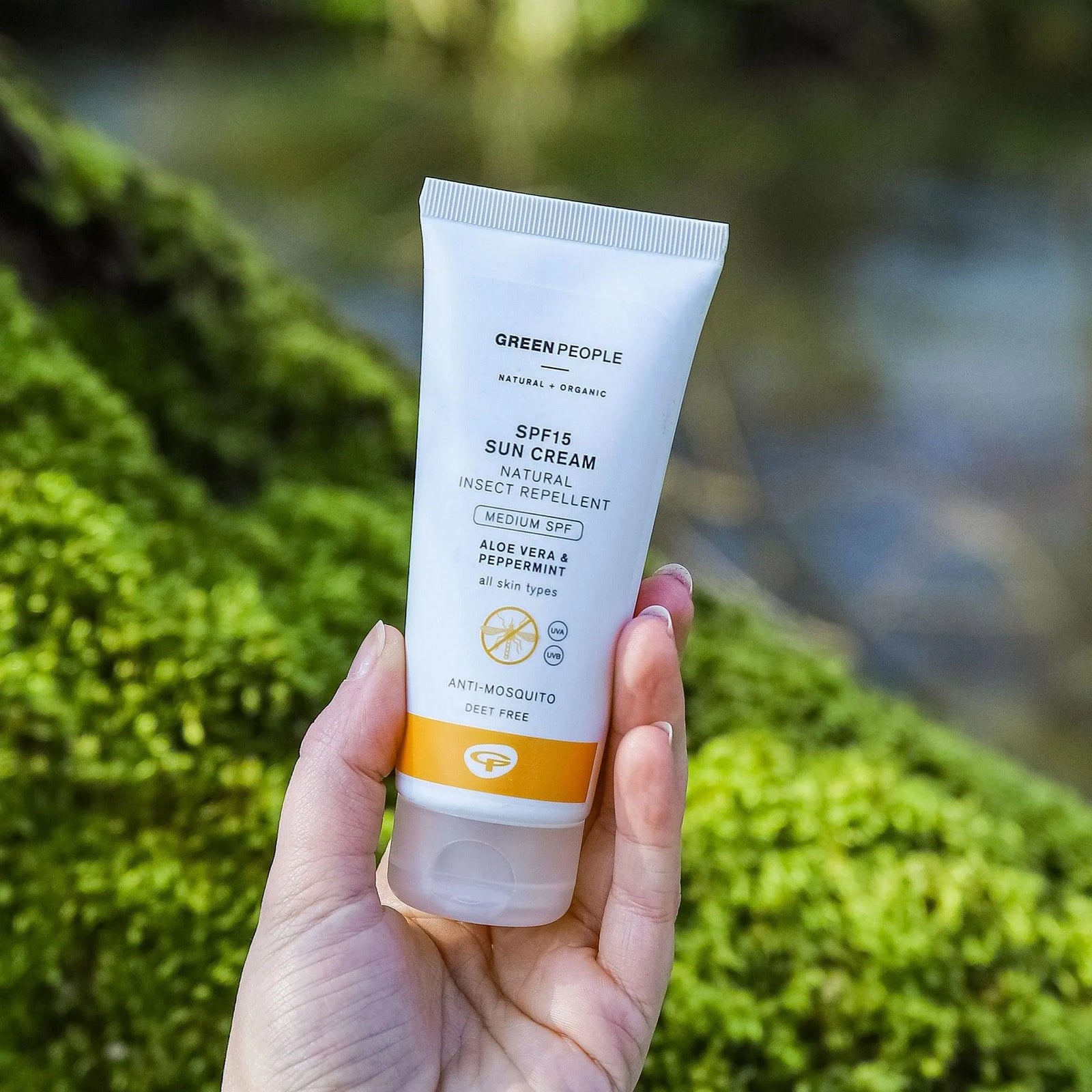 Hand holding Green People SPF15 sun cream insect repellent outdoors with green moss background