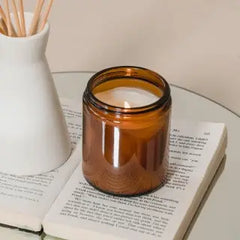 Amber glass candle jar on open book beside white vase, minimalist home decor