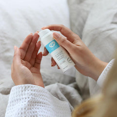 Woman applying Green People Day Solution SPF lotion on hand in cozy setting