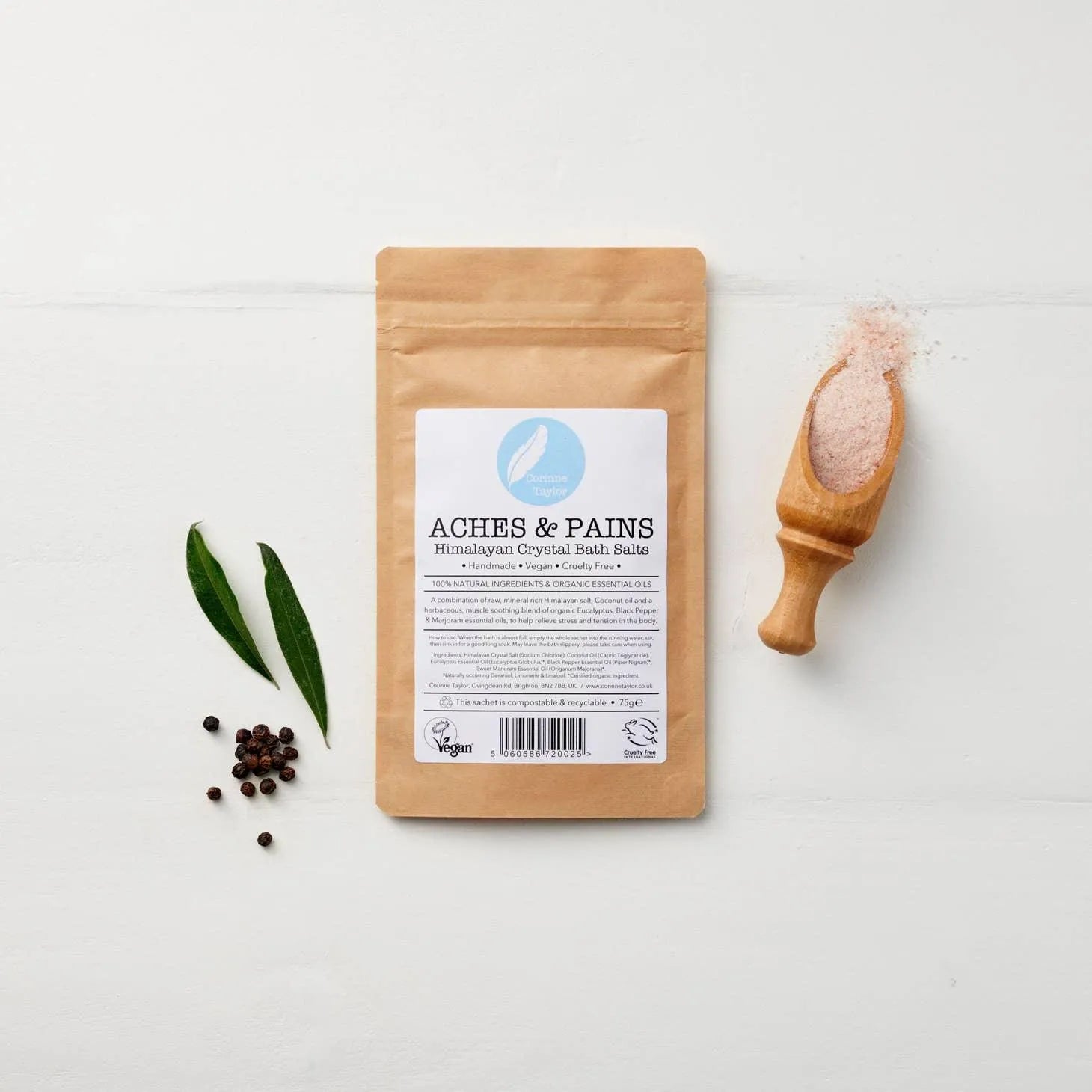 Aches & Pains Himalayan crystal bath salts pouch with wooden scoop, leaves, and peppercorns.