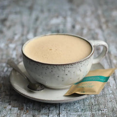 Speckled ceramic cup of frothy coffee on rustic wood with Mojo adaptogenics coffee sachet