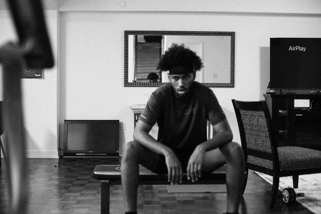 man-looks-tired-and-sits-on-black-bench-in-living-room - Ready Sweat Go