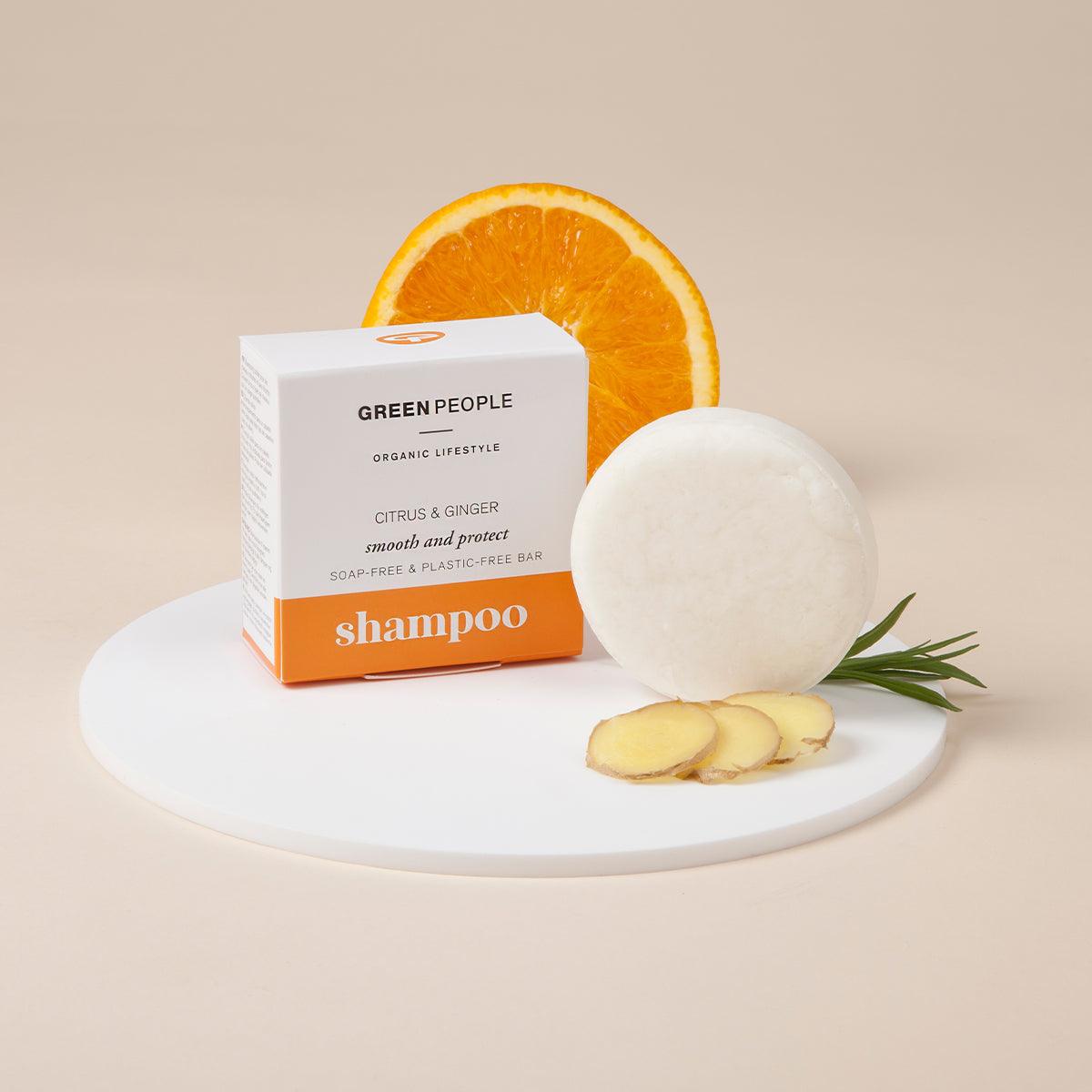 Green People citrus ginger shampoo bar with box, orange slice, ginger, and rosemary on white tray