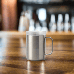 Stainless steel mug with handle on wooden bar counter, blurred background.