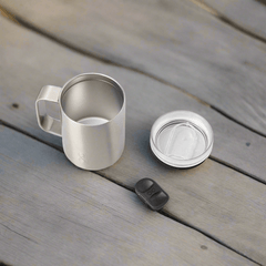 Stainless steel mug with lid and black tab on wooden surface
